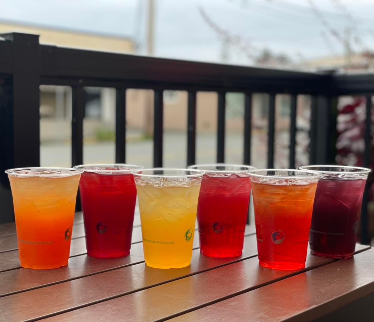 eight clear cups holding different coloured iced teas 